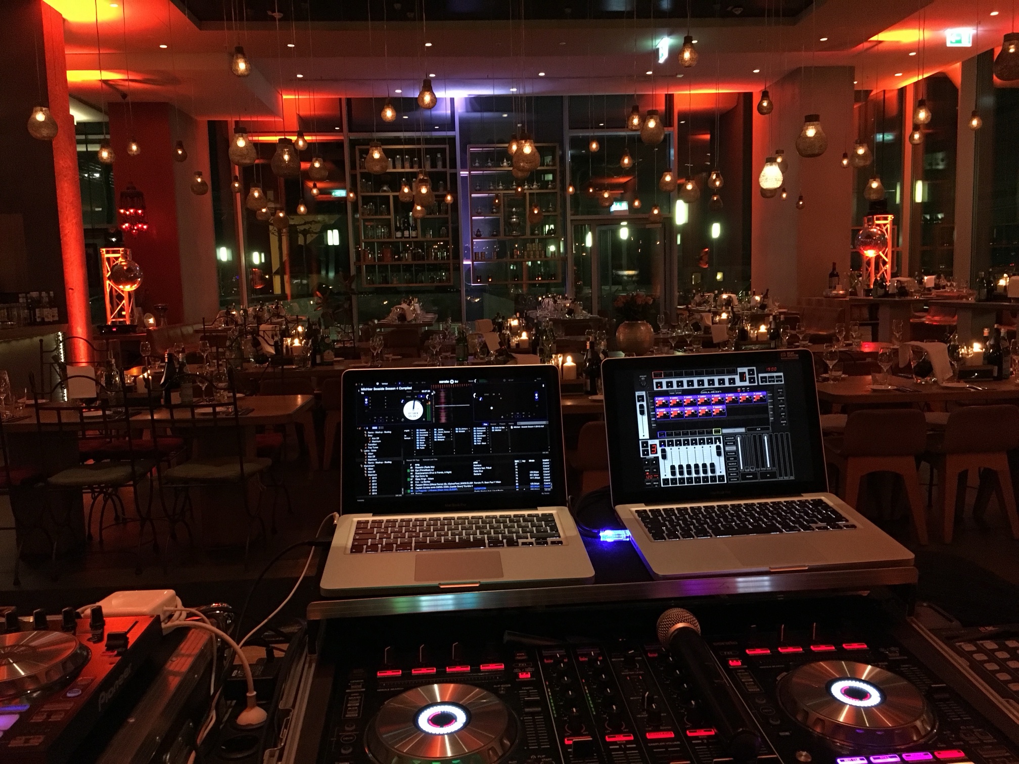 DJ-Pult von René Braun mit zwei Laptops im bona'me Köln, im Hintergrund eingedeckte Tische