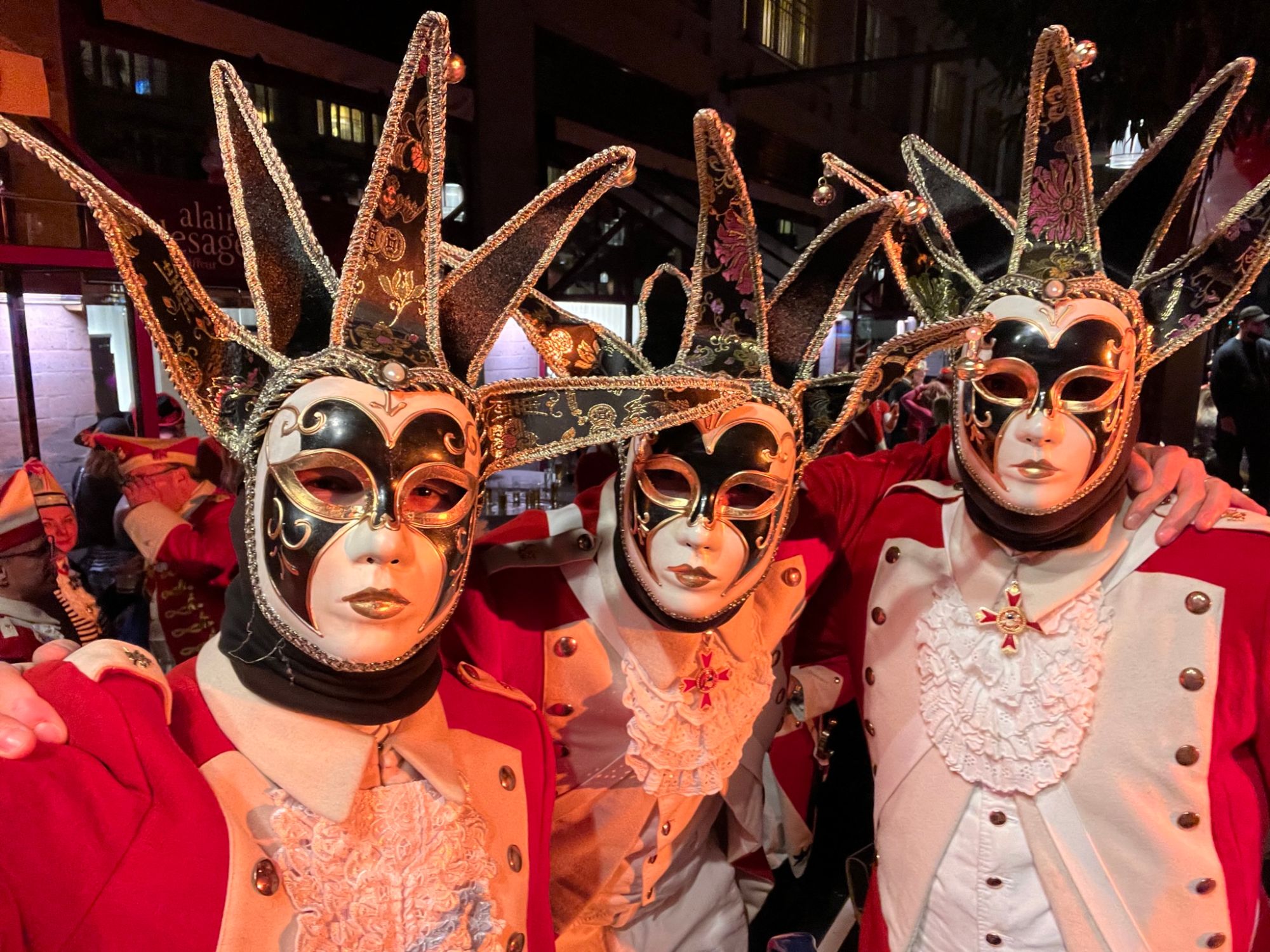 Drei maskierte Jecken in venezianischen Masken und rot-weißen Uniformen